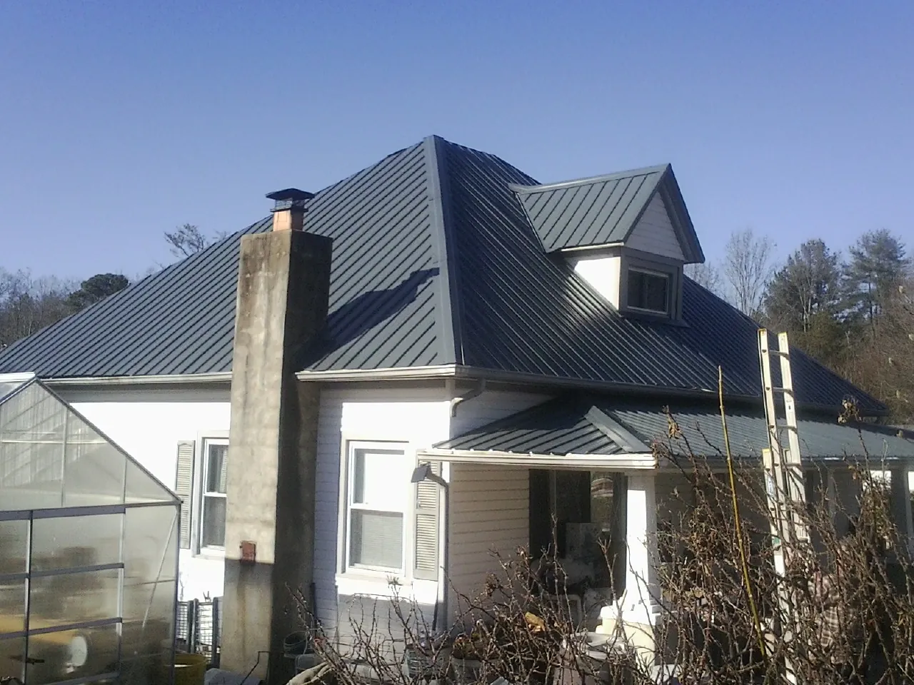 Dark blue standing seam metal roof on a white farmhouse with dormer — Slate & Tile Roof Repair by Roofing Brothers in Laneview