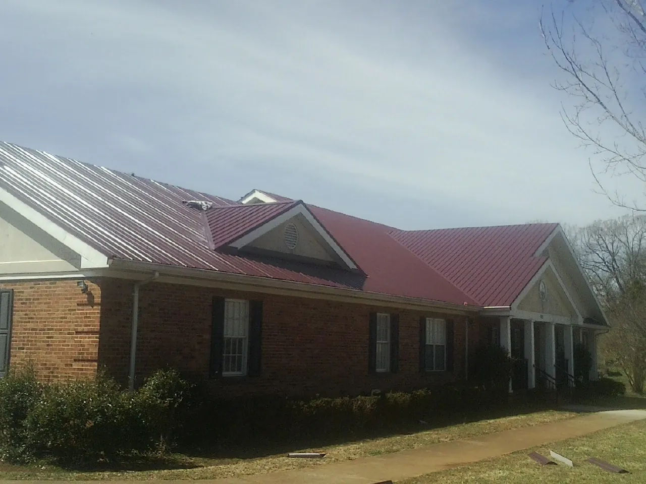 Red metal roof with gabled entries on a long brick building, from a Hail Damage Roof Repair job in Laneview