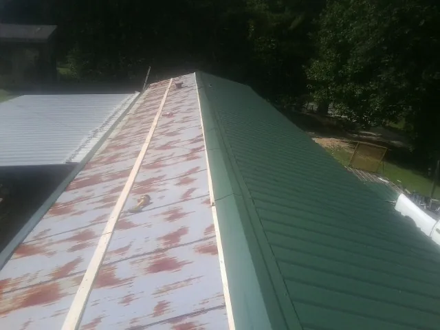 Old rusted panels beside newly installed green metal roofing — Wind Damage Roof Repair by Roofing Brothers in Laneview