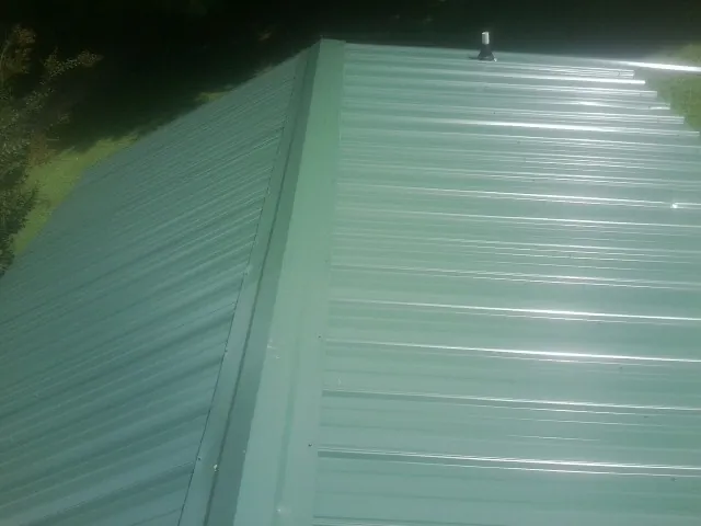 New green metal panels meeting at the ridge of a roof — Flat Roof Repair work by our crew in Laneview