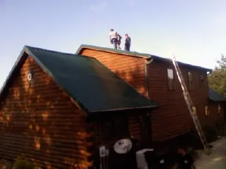 Crew on the ridge of a green metal roof on a two story log home in Laneview