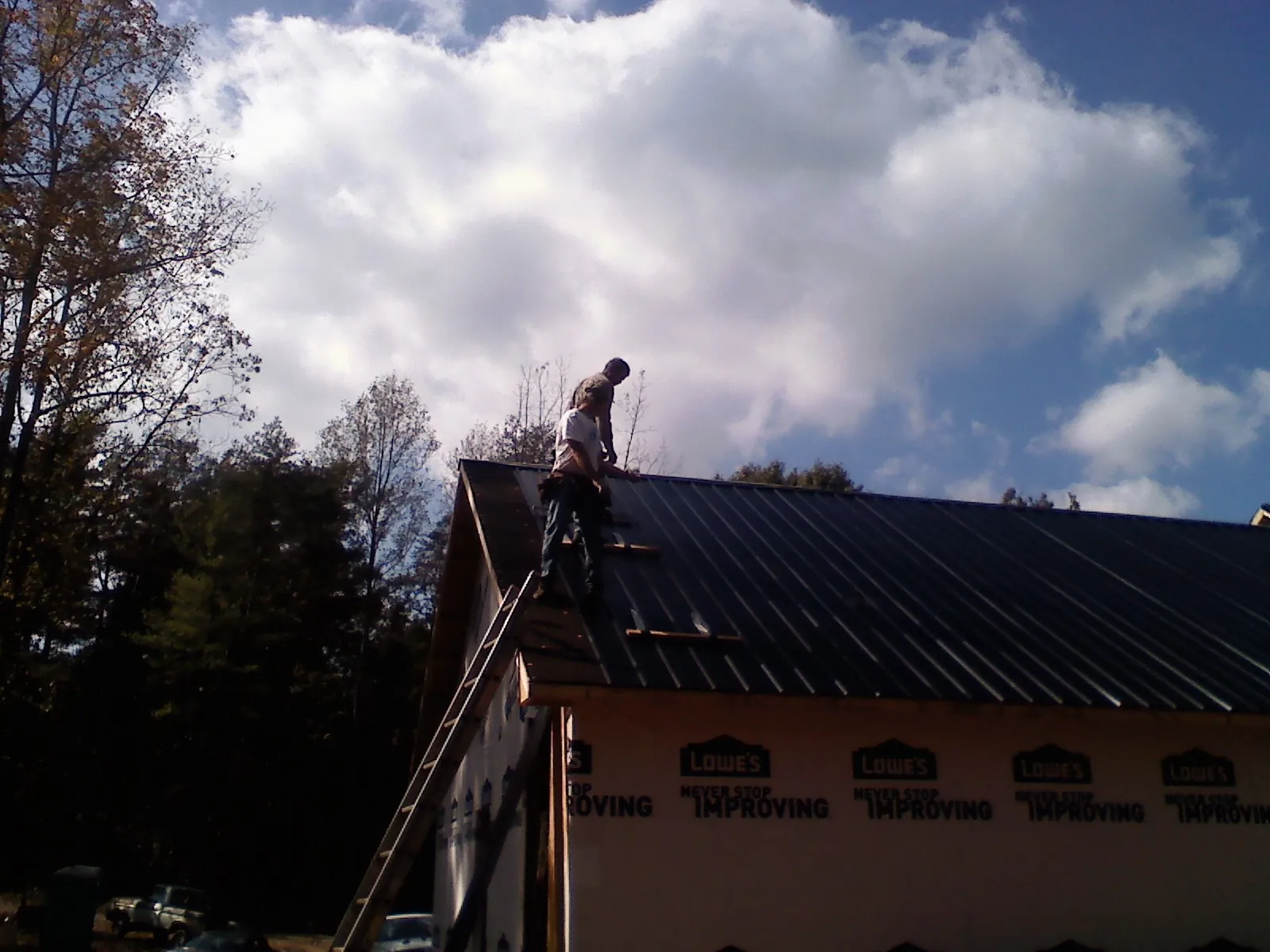 Roofer fastening dark metal panels high against a cloudy sky, from a Roof Inspection job in Laneview